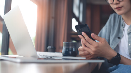 Business woman using mobile phone and working on laptop computer at coffee shop. Student searching the information, studying online, work from cafe, distant job, business casual