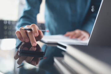 Businesswoman working on laptop computer, using mobile phone with business document, financial report on office table. Business woman busy working at modern office