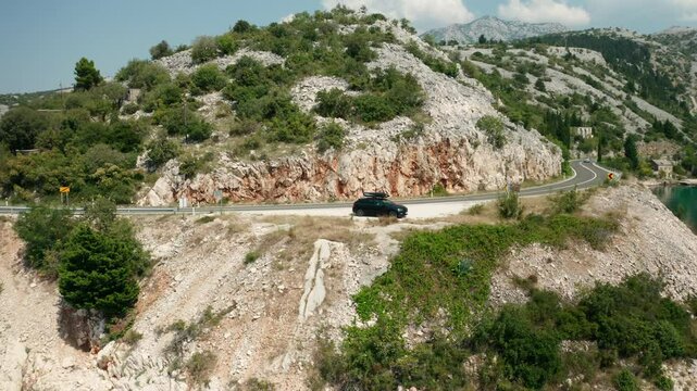  Car with a roof box stands on the side of a cliff of the sea and beautiful rocks in the background