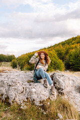 A young woman enjoys a sunny afternoon hike in the scenic mountains, wearing a sweater and hat among vibrant autumn foliage
