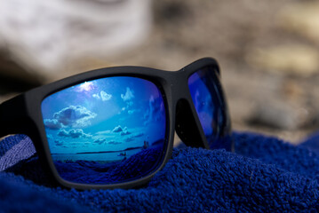 blue reflection in sunglasses by the beach on a lue towel