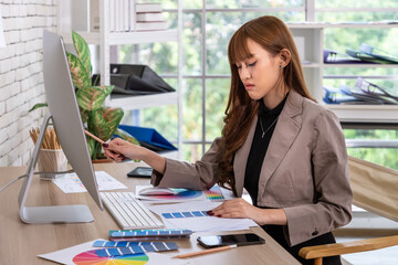 Asian female woman focused graphic designer working on creative project with color palettes at modern office workspace