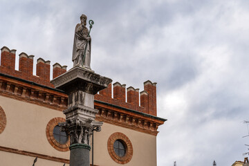 Detail of a statue of a saint at the top of a column in front a historic tower in Ravenna