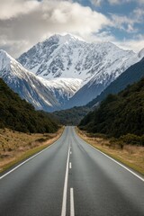 Naklejka premium Snow-capped mountains loom over a winding road in a serene valley