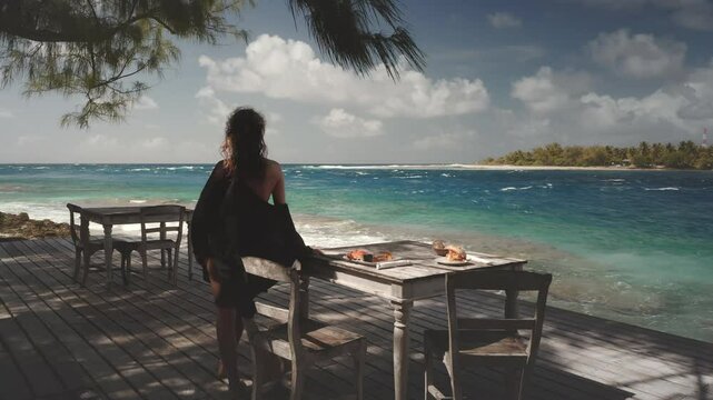 Tourist is enjoying a moment of peace and relaxation at a wooden restaurant table, savoring the breathtaking view of the turquoise ocean