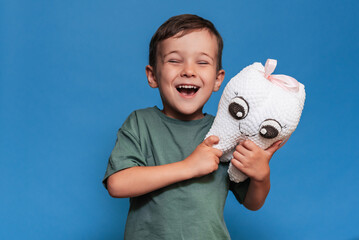 A smiling boy with healthy teeth holds a plush tooth on a blue background. Oral hygiene. Pediatric...