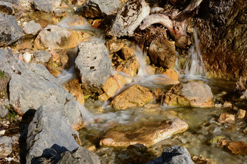 Several streams of a small waterfall flow over the stones of the mountain rocks. Natural landscape. Long exposure