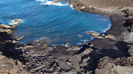 Atlantic ocean with waves and black basalt sand and rocks, view from above from a drone.