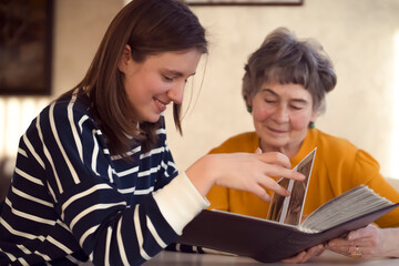 Obraz premium An old woman and her granddaughter look at photos from the family album/