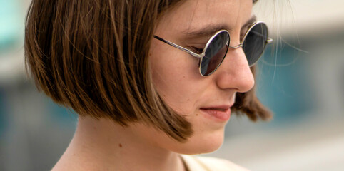 A stylish young girl in black sunglasses walks in a city, portrait closeup.