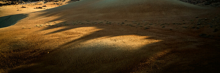 A desert landscape with sandy valleys among mountains and volcanoes at sunset.