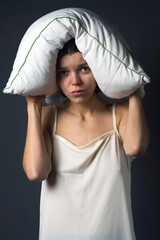 A young tired amusing girl holds a pillow on her head with her hands. Loud noises from neighbors at...