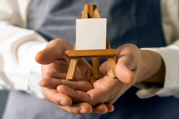 Artist holds a small easel in his hands, closeup view.