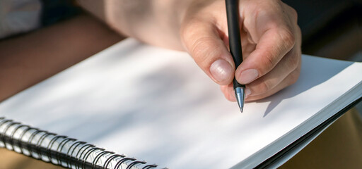 A male hand holds a pen and writes in a sketchbook, notepad closeup.