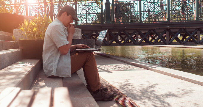 A man is sitting in a park and working on a laptop outdoors.