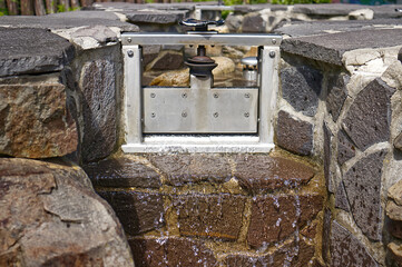 Detail of a small stainless steel sluice in a stone river bed. Technology, retention of water flow.