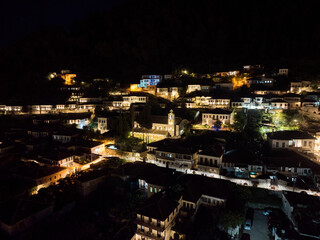 Cityscape panorama of historical Albanian city of Berat and its Ottoman style houses with city lights, Albania. Aerial drone photo taken at night - evening
