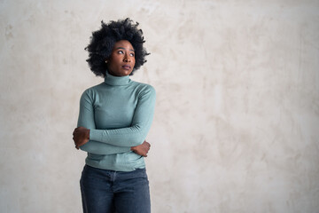 A professional black standing with her arms crossed, wearing a turquoise turtleneck and jeans...