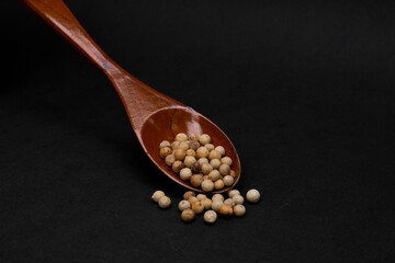 White Pepper on a wooden spoon on a black background. one of the most considered spices in a dish.