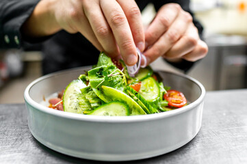 Close-up of hands garnishing a fresh salad with microgreens in a white bowl. The vibrant colors of vegetables and greens highlight freshness and appeal of dish. Perfect for healthy eating concepts.