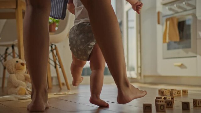 A baby learns to walk new stage in raising children. Little feet make their first movements. A loving mother slowly leads her child, holding his hands. A young woman helps the baby master a new skill