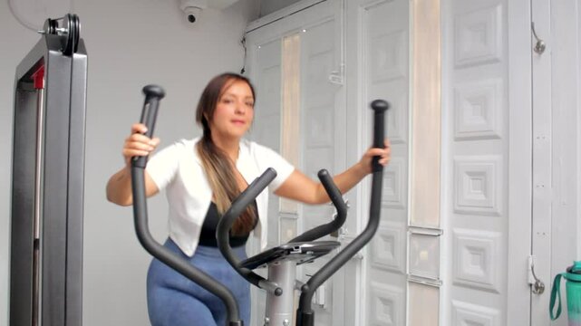 Happy young fitness woman exercising on an elliptical machine in a gym