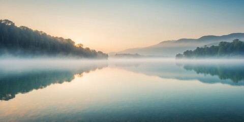Obraz premium A serene lake at sunrise with mist hovering over the surface.