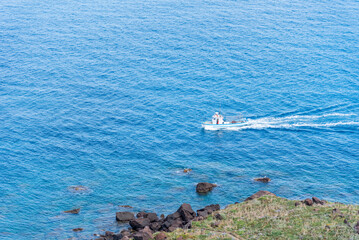 Calm, blues sea near Sardinian coast, panorama with small fishing boat sailing toward home port.