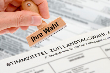 Ein Holzstempel ist beschriftet mit dem Aufdruck: Ihre Wahl über einem Stimmzettel zur Landtagswahl