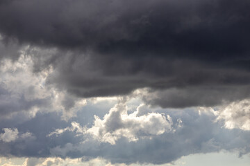 Obraz premium Beautiful dramatic sky background with stormy clouds before a thunderstorm with sunlight. Dark gray clouds floating in the bright sunny sky.