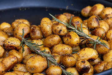 Close-up of roasted potatoes seasoned with a blend of aromatic herbs and spices, drizzled with olive oil, and garnished with rosemary and salt. Food concept