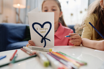 Children creating handmade Father's Day card with markers and colored pencils on table with love...