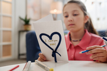 Young girl creating handmade Father Day card with heart design and inscription I Love You Dad on...