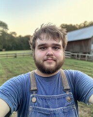 Young Man in Overalls Stands on a Farm at Sunset With a Bearded Look