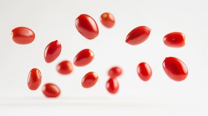 Multiple red cherry tomatoes falling against a white background.