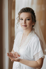 A woman in a white robe is holding a ring in her hand. She is wearing a veil and has her hair in a bun. Concept of elegance and sophistication, as the woman is dressed in a wedding-like attire