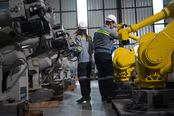 Engineer with helmet safety standing by robotic arm and operating machine in industry factory, technician worker check for repair maintenance electronic operation