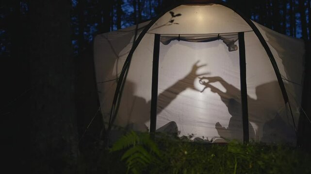 Children making shadow puppets in a camping tent at night