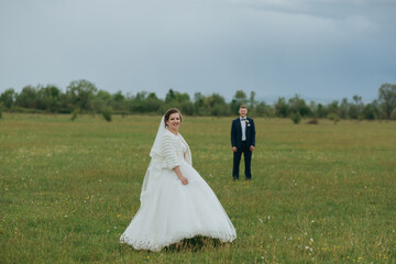 A bride and groom are standing in a field, with the bride wearing a white dress and the groom wearing a suit. Scene is romantic and happy, as the couple is getting married