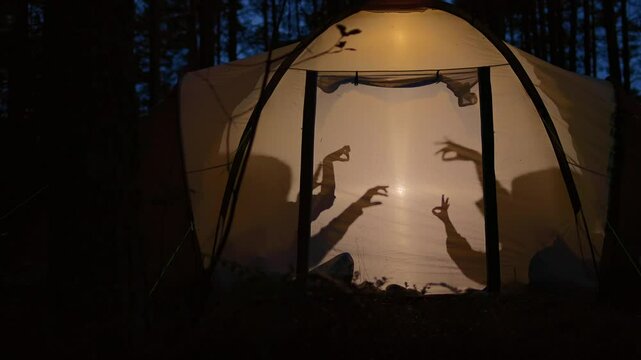 Children making shadow puppets in a camping tent at night