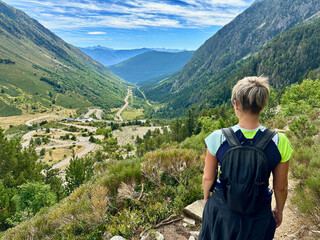 A woman hiker stands at a vantage point overlooking the winding road through the Gerber Valley in the Catalan Pyrenees.