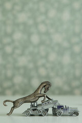 A close-up of an antique bronze figurine in profile of a horse trampling metal toy cars, creating...