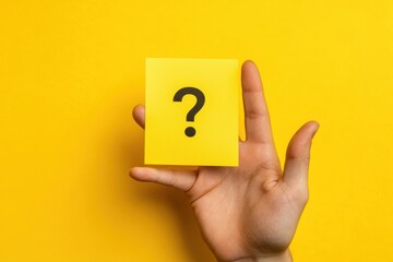 Hand holding yellow sticky note with black question mark