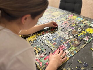 Caucasian girl in white shirt solving colorfull jigsaw puzzle game on table