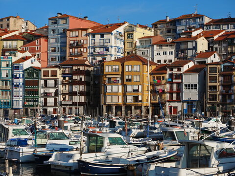 Puerto y casas de colores de la ciudad de Bermeo con sus barcos, lanchas motoras y botes de pescadores rodeado de estatuas de bronce y flotador marinero  de socorro