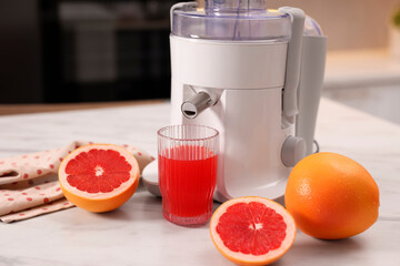 Modern juicer, fresh grapefruits and glass on white marble table in kitchen