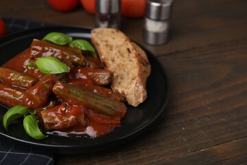 Tasty stew with okra, tomato sauce, bread and basil on wooden table, closeup. Space for text