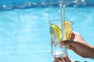 Woman holding tasty cocktail in glass near swimming pool outdoors, closeup