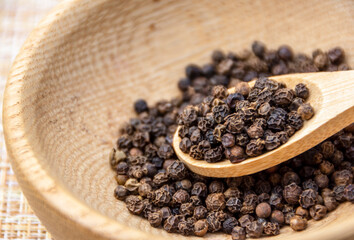 Dry black pepper spice on a wooden spoon close up. Black peppercorns.