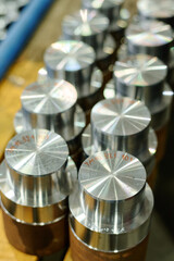 Close-up of freshly machined metallic parts arranged in a line on factory workbench catching light from nearby sources. Parts display clean surfaces with reflective finishes